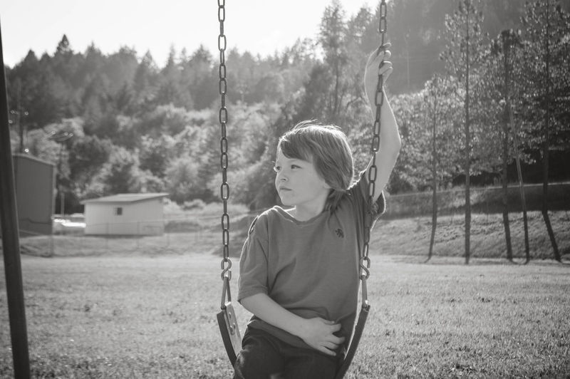 Cute boy looking away while sitting on swing at playground