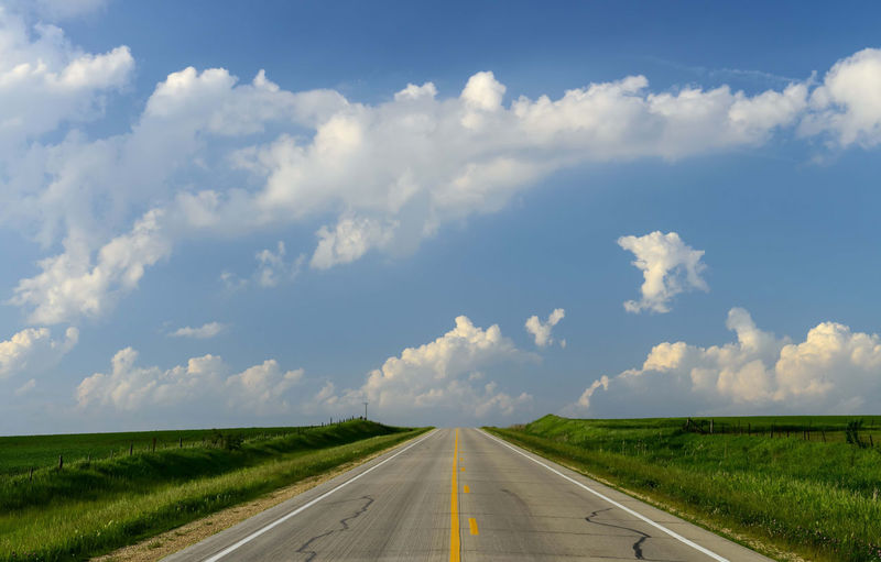 Empty road amidst field against sky