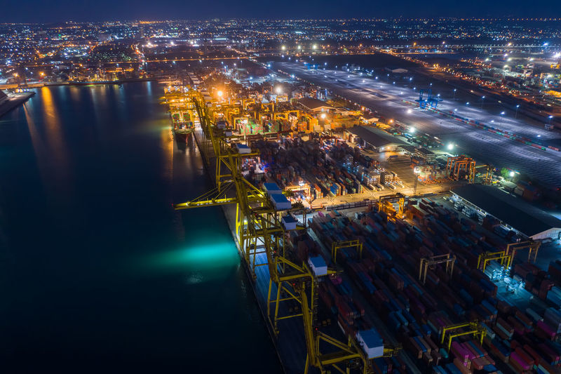 High angle view of shipping container and terminal illuminated buildings by sea at night