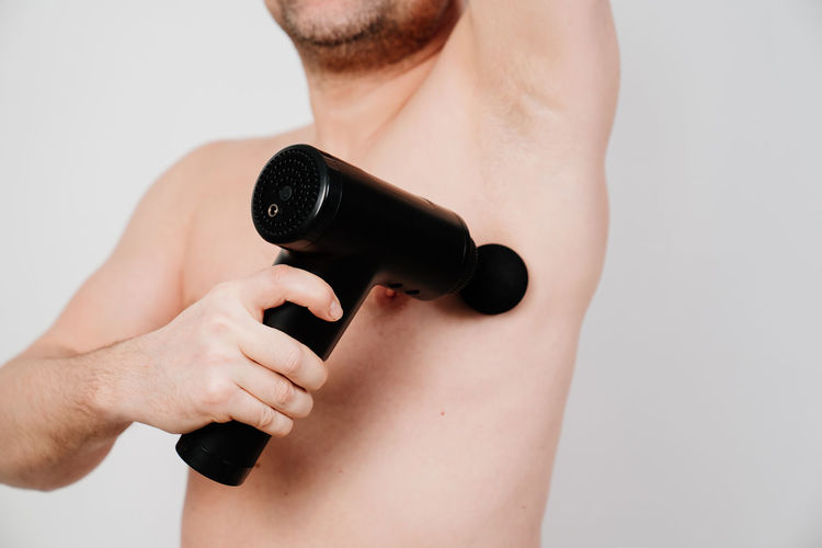 Midsection of shirtless man using percussion massager