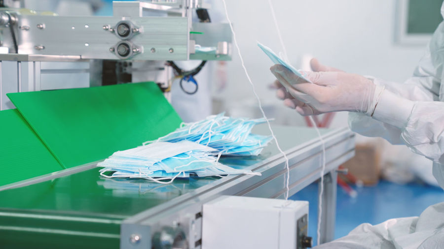 Midsection of person manufacturing mask at factory