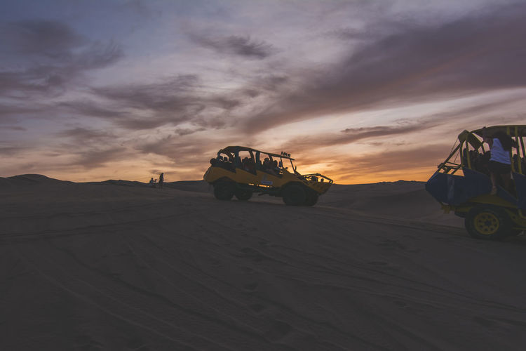 Tourists in dune buggy on sand at dusk