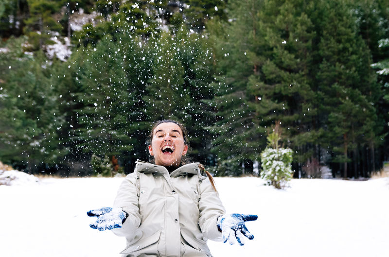 Smiling woman throwing snow mid air during winter