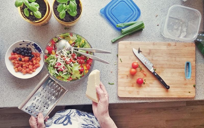Cropped image of woman grating cheese over salad in kitchen