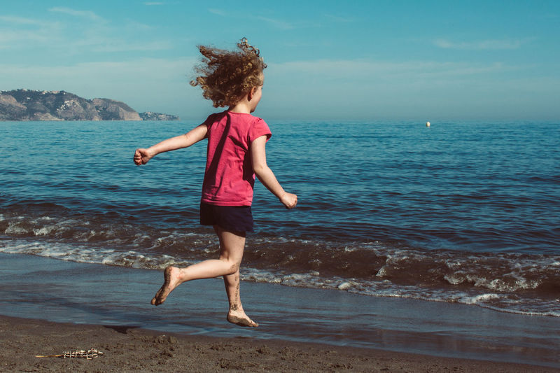 Full length of girl running at beach against sky