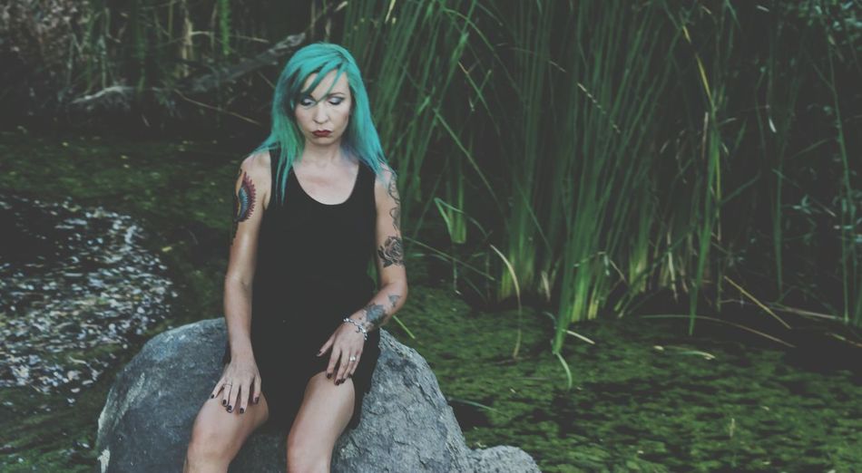 Punk woman sitting on rock against plants in pond