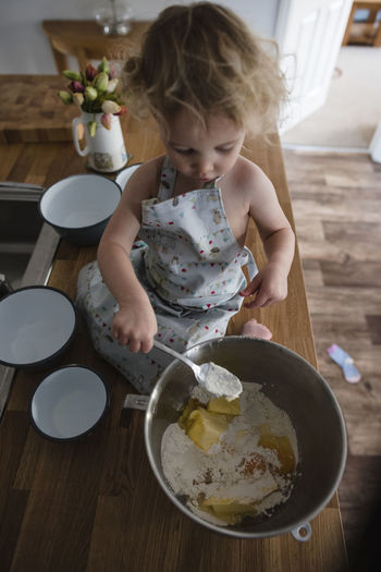 High angle view of girl mixing batter in bowl while sitting on kitchen counter
