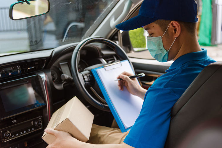 Delivery person wearing mask writing while sitting in car
