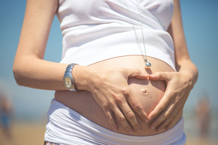 Midsection of pregnant woman making a heart shape sign