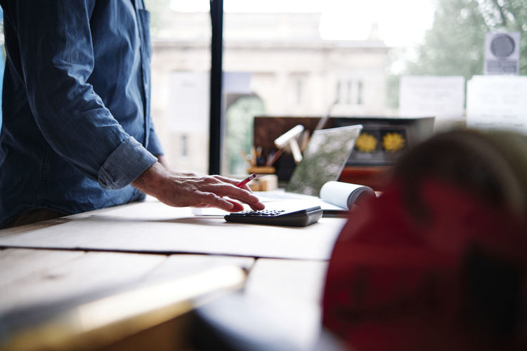 Male store owner using calculator while making financial bill in workshop
