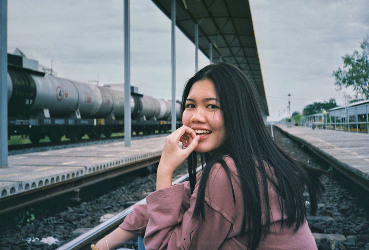Portrait of smiling young woman sitting on railroad track