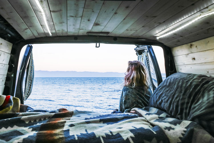 Rear view of woman looking at sea while leaning against travel trailer