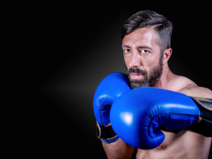 Portrait of boxer wearing blue gloves against black background