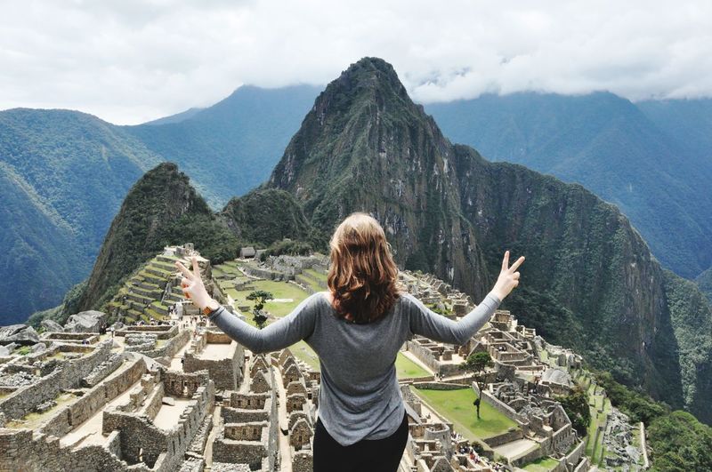 Rear view of woman with arms outstretched standing on mountain against sky