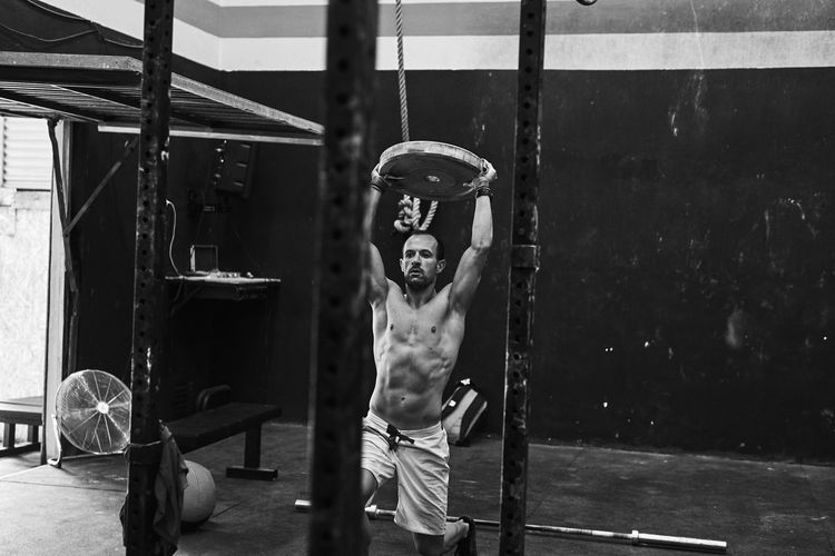 Fit shirtless young man working out with heavy disc in a garage