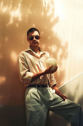 Young man wearing sunglasses standing against wall