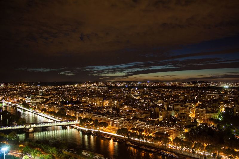 Illuminated cityscape by seine river against cloudy sky at night