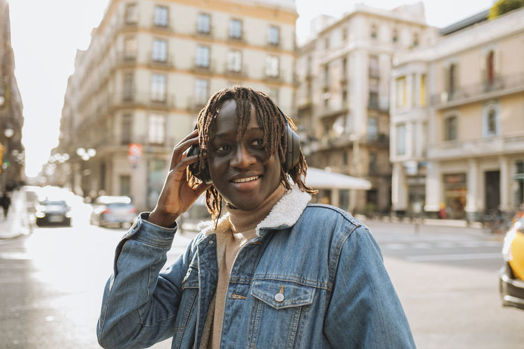 Smiling man listening music through headphones in city
