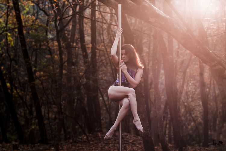 Woman dancing on pole against trees in forest
