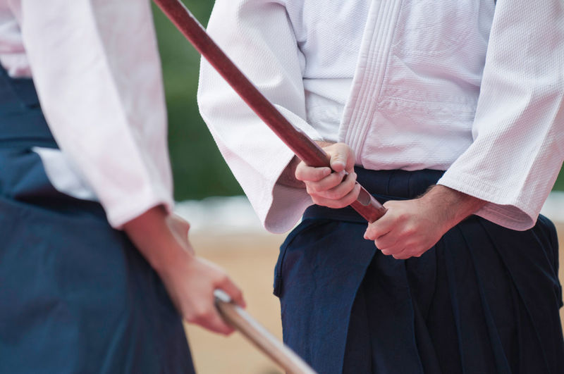 Midsection of men holding sticks