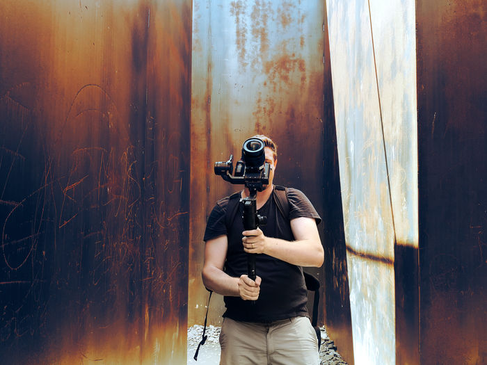 Man holding camera standing against rusty metal wall