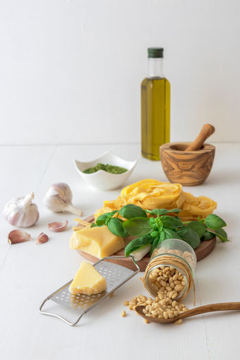 Low angle view of basil pesto with ingredients and raw pasta on white wooden table background
