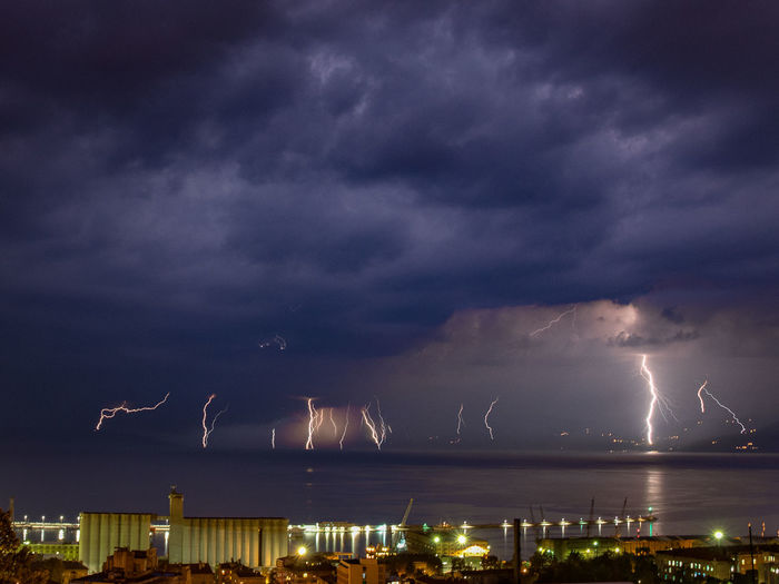 Lightning over sea by illuminated city at night