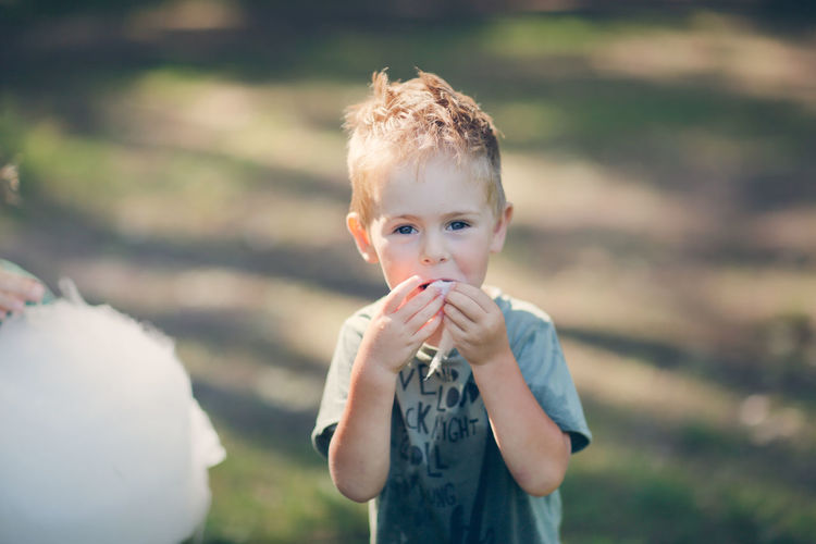 Cute european boy eating cotton candy in the park, lifestyle