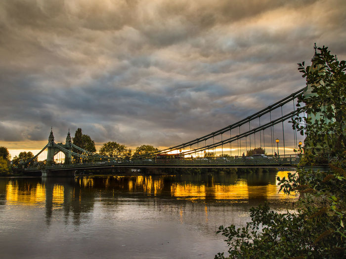 Hammersmith bridge over river against cloudy sky
