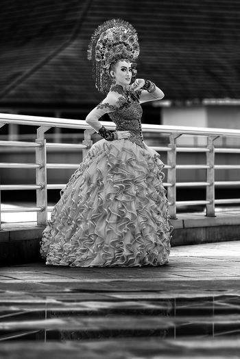 Portrait of young woman in dress standing on footpath by railing