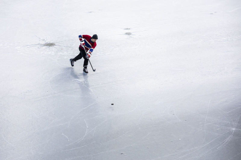 Hockey player skating and shooting puck on ice playing pond hockey