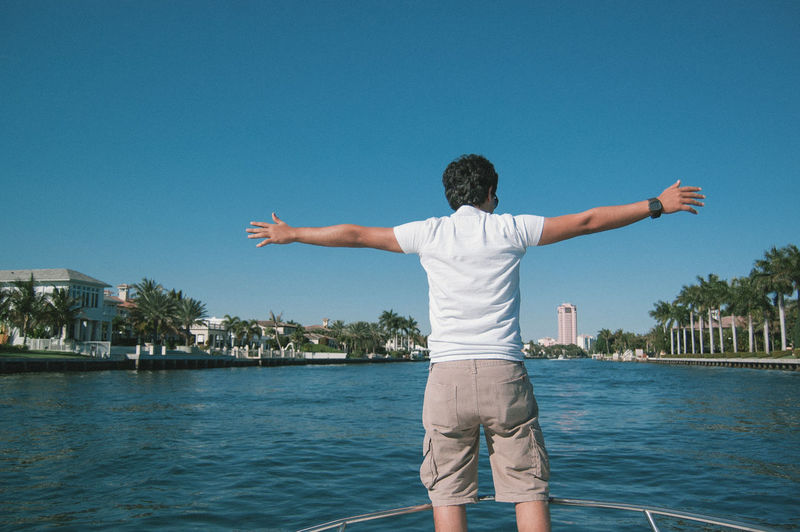 Rear view of man with arms outstretched on boat in lake