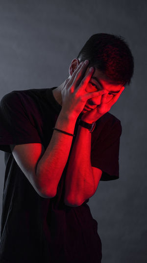 Portrait of young man covering face while standing against gray background