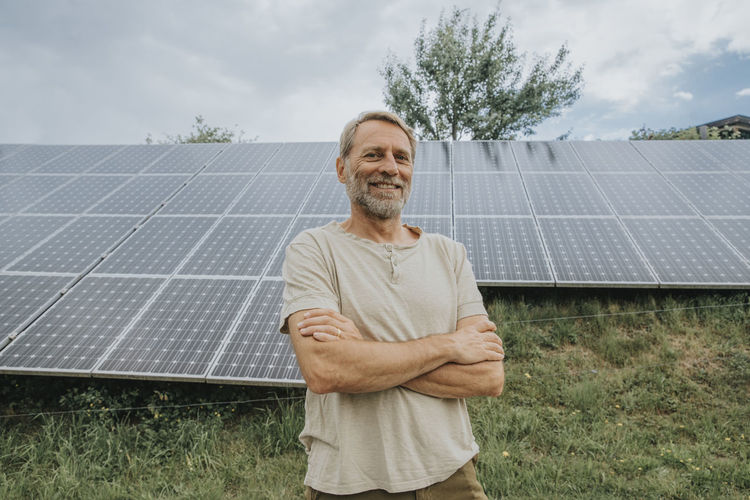 Smiling man with arms crossed in front of solar panels
