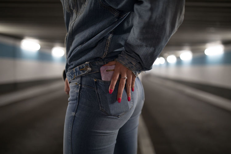 Midsection of woman holding phone pocket while standing in illuminated tunnel