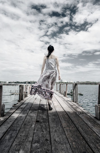 Rear view of woman on pier against sky