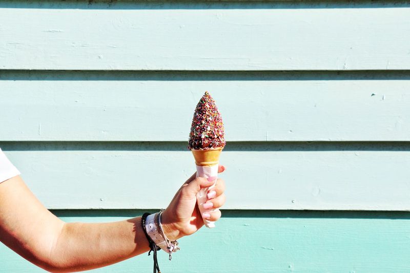 Midsection of person holding ice cream against wall