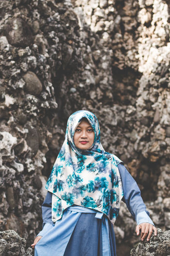 Portrait of woman wearing hijab sitting against rock formation