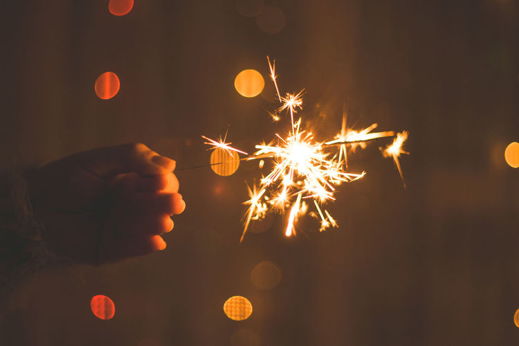 Cropped hands of woman holding lit sparkler at night