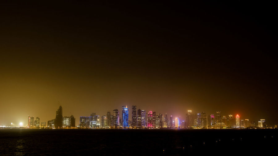 Illuminated buildings of doha against sky at night
