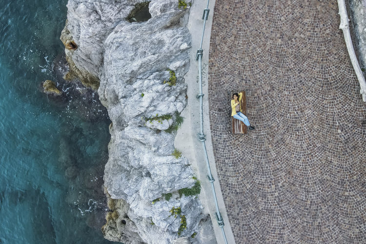 Italy, apulia, erchie, aerial view of young woman lying on bench overlooking amalfi coast