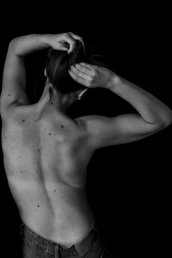 Rear view of shirtless woman standing against black background