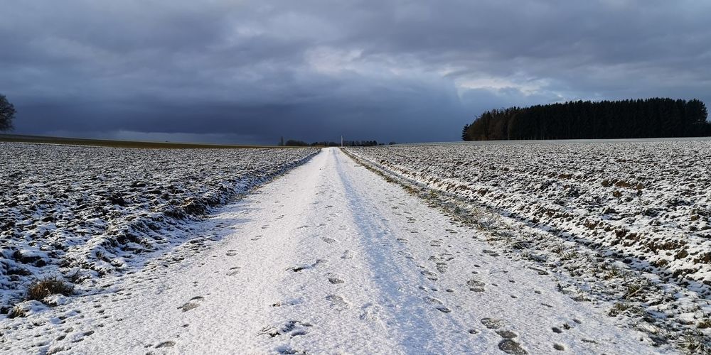 Empty road on snow covered land against sky