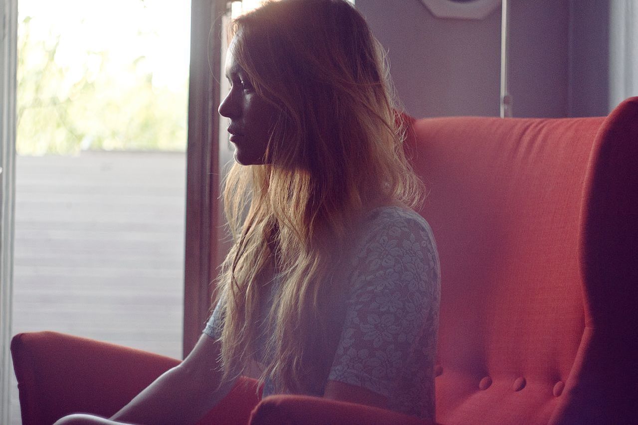 indoors, lifestyles, young adult, young women, long hair, leisure activity, person, waist up, window, home interior, casual clothing, headshot, sitting, side view, contemplation, rear view