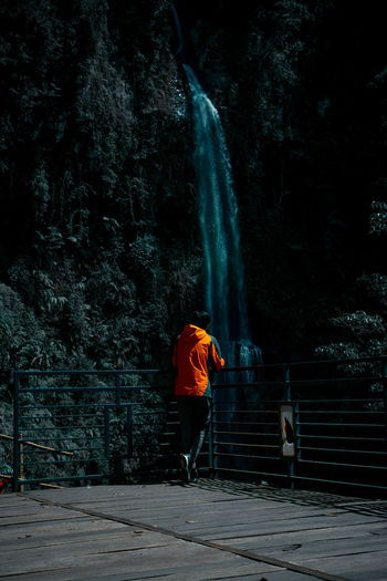 Rear view of man standing by railing against waterfall