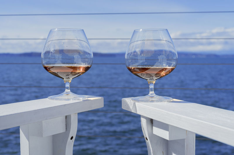 Close-up of brandy snifters on white adirondack chairs against sea