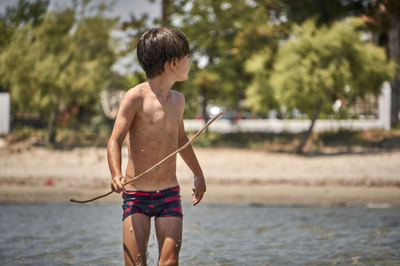 Shirtless boy holding stick while standing in lake