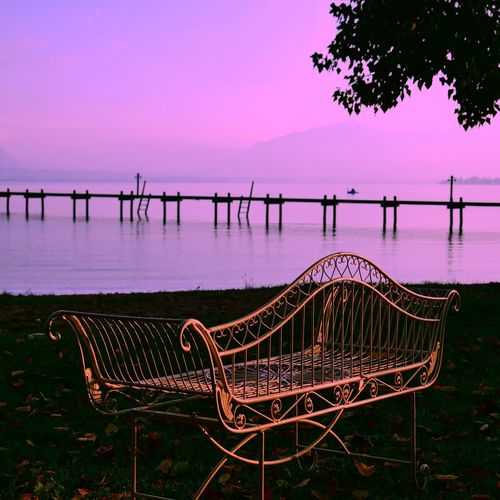 Empty chair by lake against sky during sunset