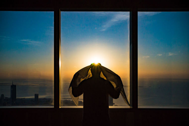 Rear view of silhouette man standing against window