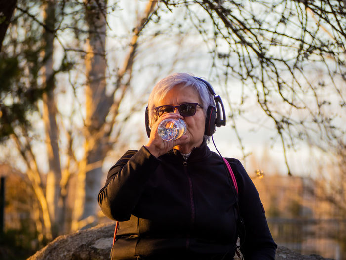 Senior woman drinking water from bottle in park during sunset